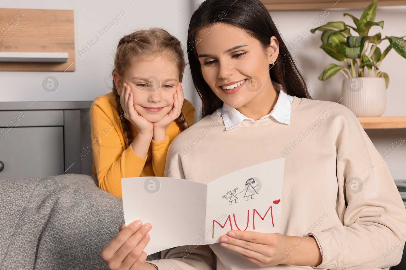 Photo of Happy woman receiving greeting card from her little daughter at home