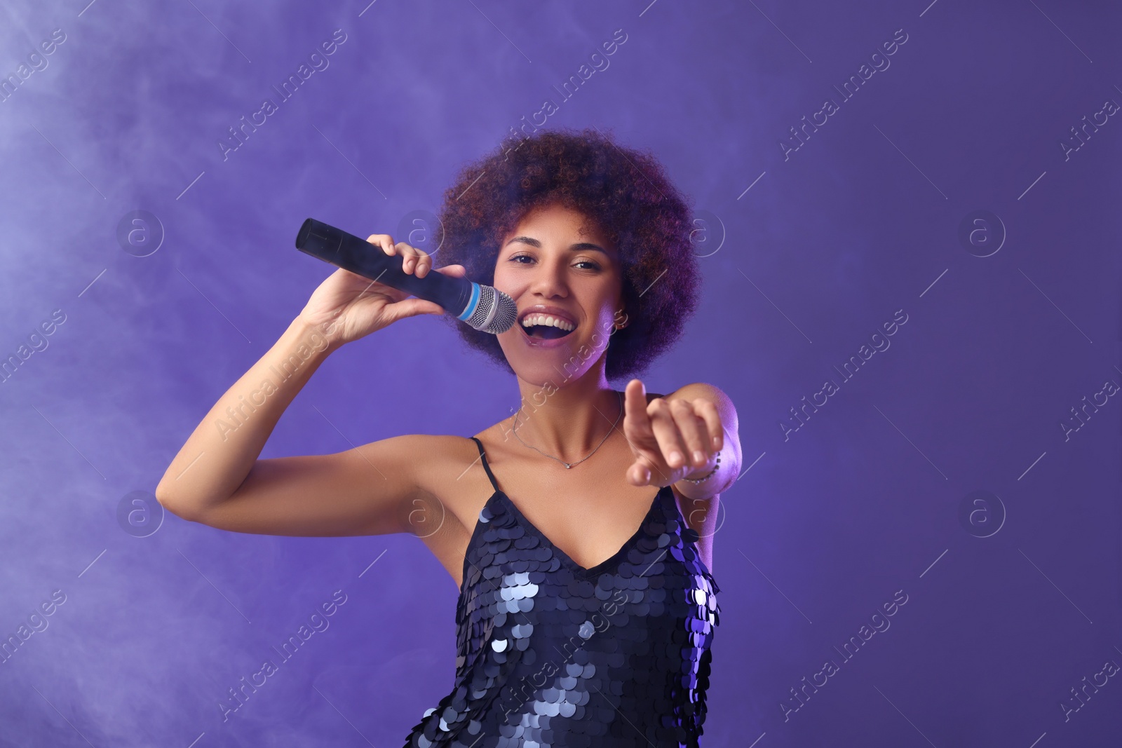 Photo of Curly young woman with microphone singing on purple background