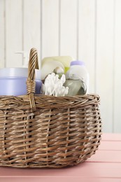 Photo of Wicker basket full of different baby cosmetic products and bathing accessories on pink wooden table, closeup