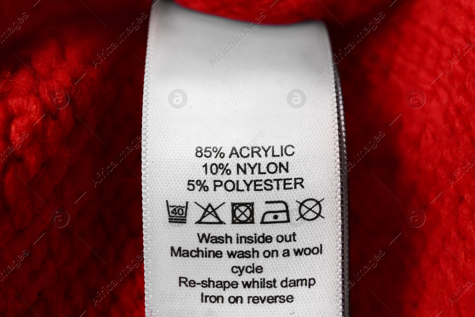 Photo of Clothing label with care symbols and material content on red sweater, closeup view