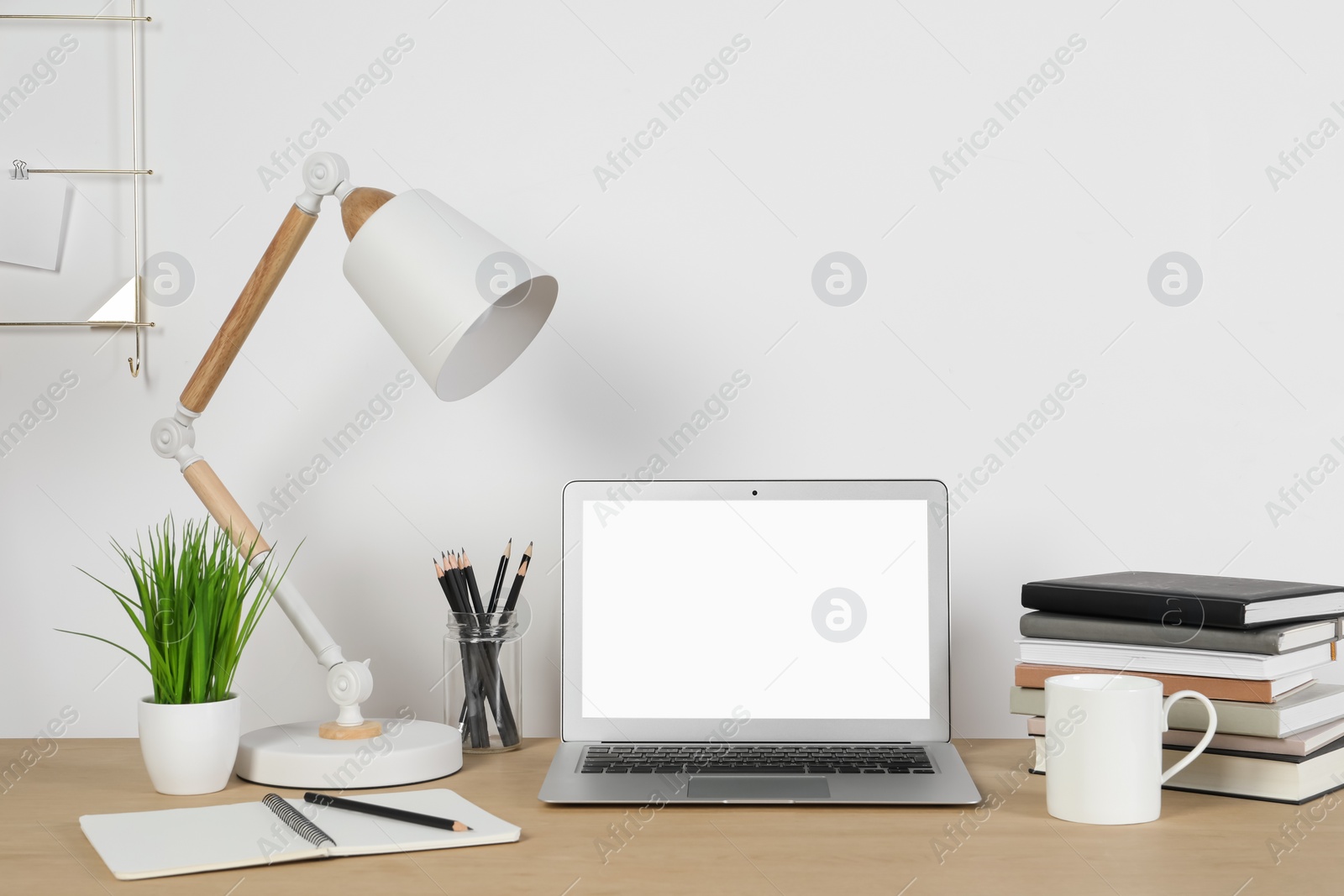 Photo of Cozy workspace with laptop, lamp and stationery on wooden desk at home