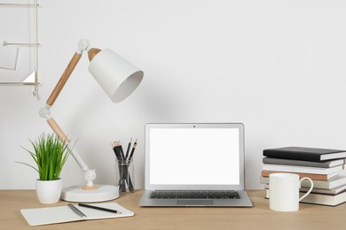 Cozy workspace with laptop, lamp and stationery on wooden desk at home