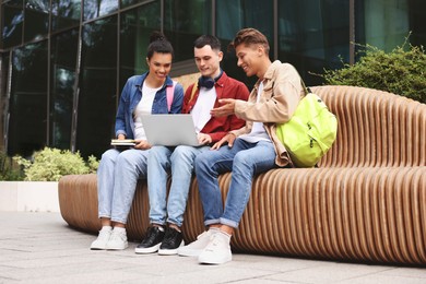 Photo of Happy young students studying with laptop on bench outdoors