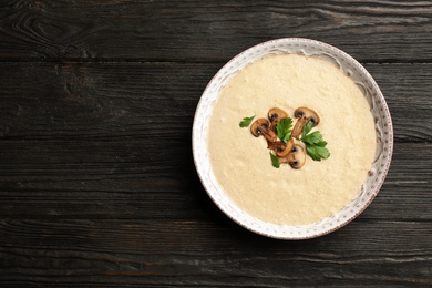 Bowl of fresh homemade mushroom soup on wooden background, top view with space for text