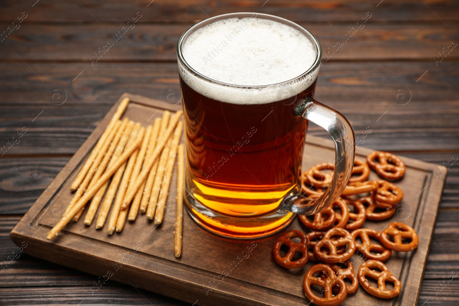 Photo of Delicious pretzel crackers, salted sticks and mug of beer on wooden table