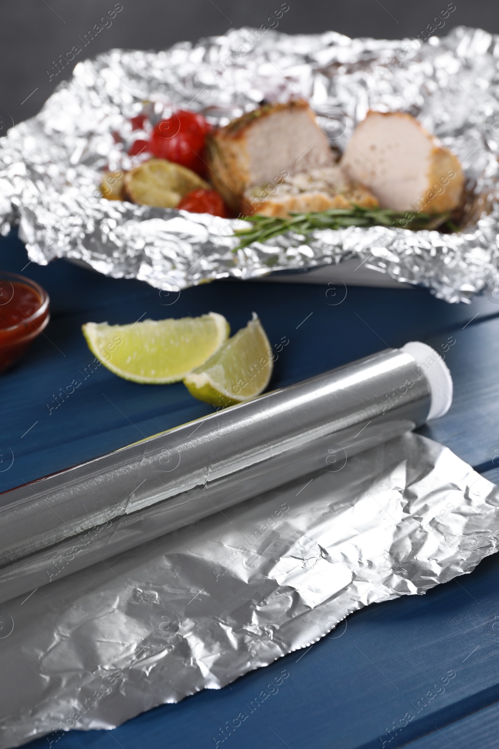 Photo of Aluminum foil and pieces of delicious meat with tomatoes on wooden table, selective focus