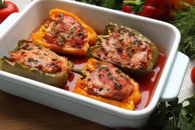 Photo of Tasty stuffed peppers in dish and ingredients on table, closeup