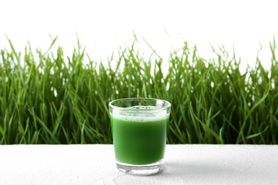 Photo of Glass of juice on table and fresh wheat grass against white background