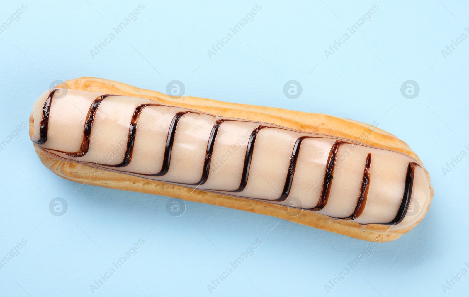 Photo of Delicious eclair covered with glaze on light blue background, top view