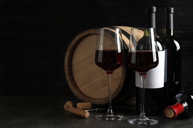 Composition with glasses and bottles of red wine on table against dark background. Space for text