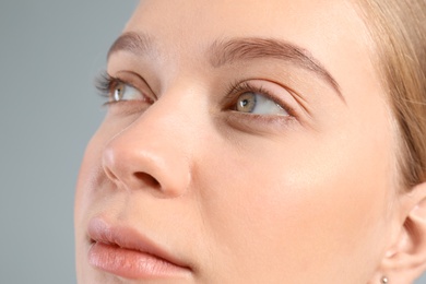 Young woman with beautiful natural eyelashes on gray background, closeup