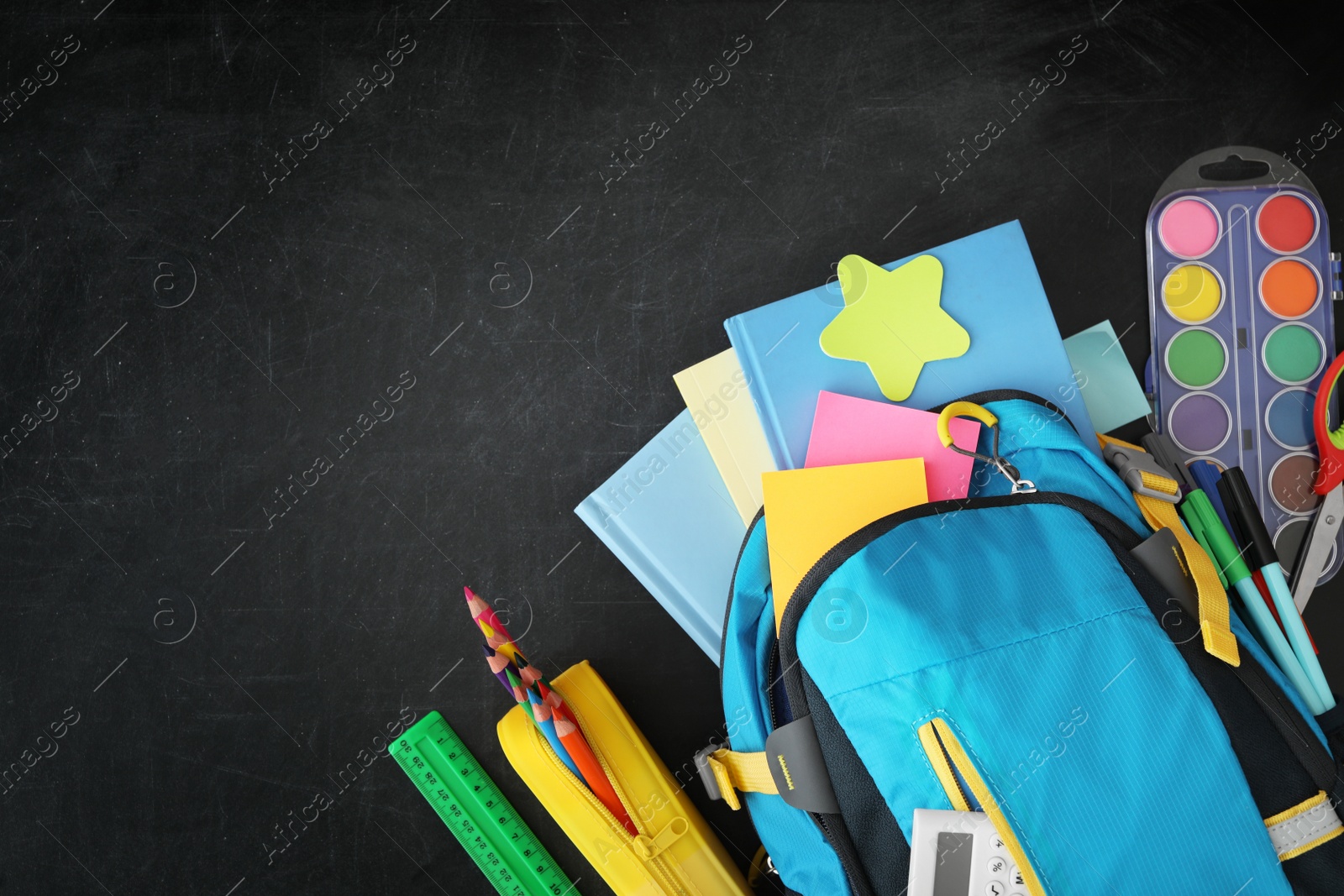 Photo of Blue backpack and different stationery on blackboard, flat lay with space for text. Back to school