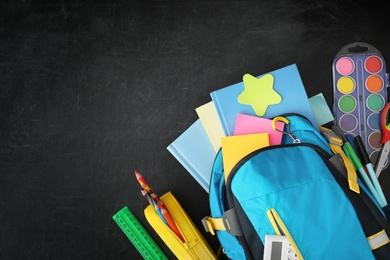Photo of Blue backpack and different stationery on blackboard, flat lay with space for text. Back to school