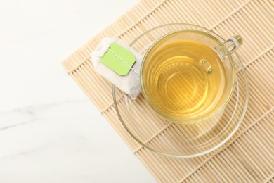 Tea bag and glass cup of hot beverage on white table, top view. Space for text