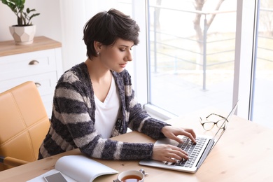 Photo of Young woman working with laptop at desk. Home office