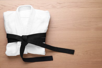 Photo of Martial arts uniform with black belt on white wooden background, top view. Space for text