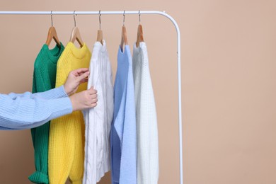 Photo of Woman taking sweater from rack on beige background, closeup. Space for text