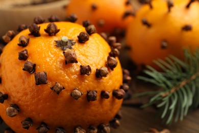 Photo of Pomander balls made of tangerines with cloves and fir branch on wooden table, closeup