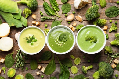 Photo of Flat lay composition with different fresh vegetable detox soups made of green peas, broccoli and spinach in dishes on wooden background