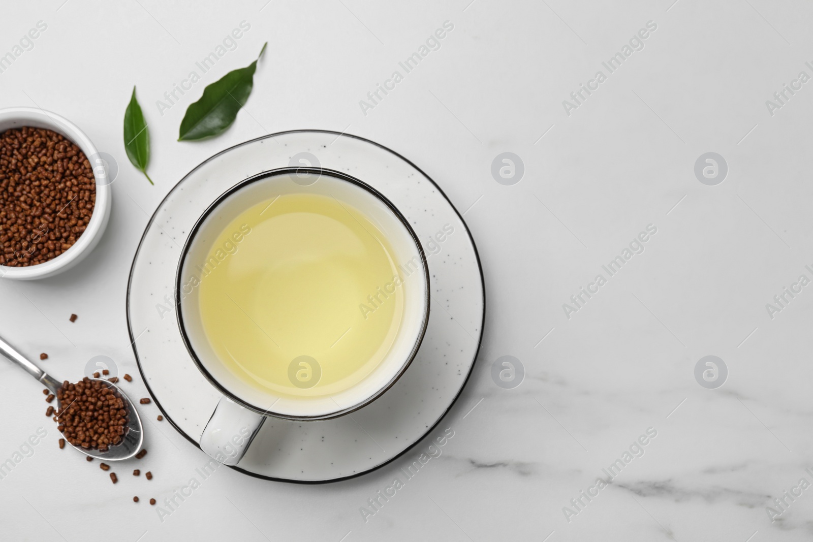Photo of Cup of buckwheat tea and granules on white marble table, flat lay. Space for text