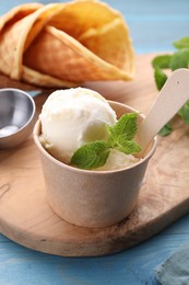 Photo of Delicious vanilla ice cream with mint in paper cup on light blue wooden table