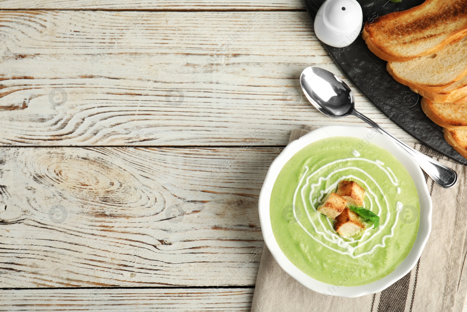 Photo of Delicious broccoli cream soup with croutons served on white wooden table, flat lay. Space for text