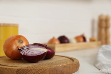 Photo of Fresh cut and whole onions on wooden board in modern kitchen, closeup. Space for text