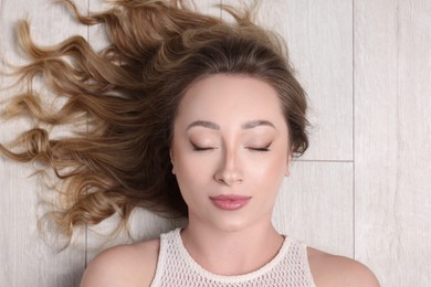 Portrait of beautiful woman with closed eyes on wooden floor, top view