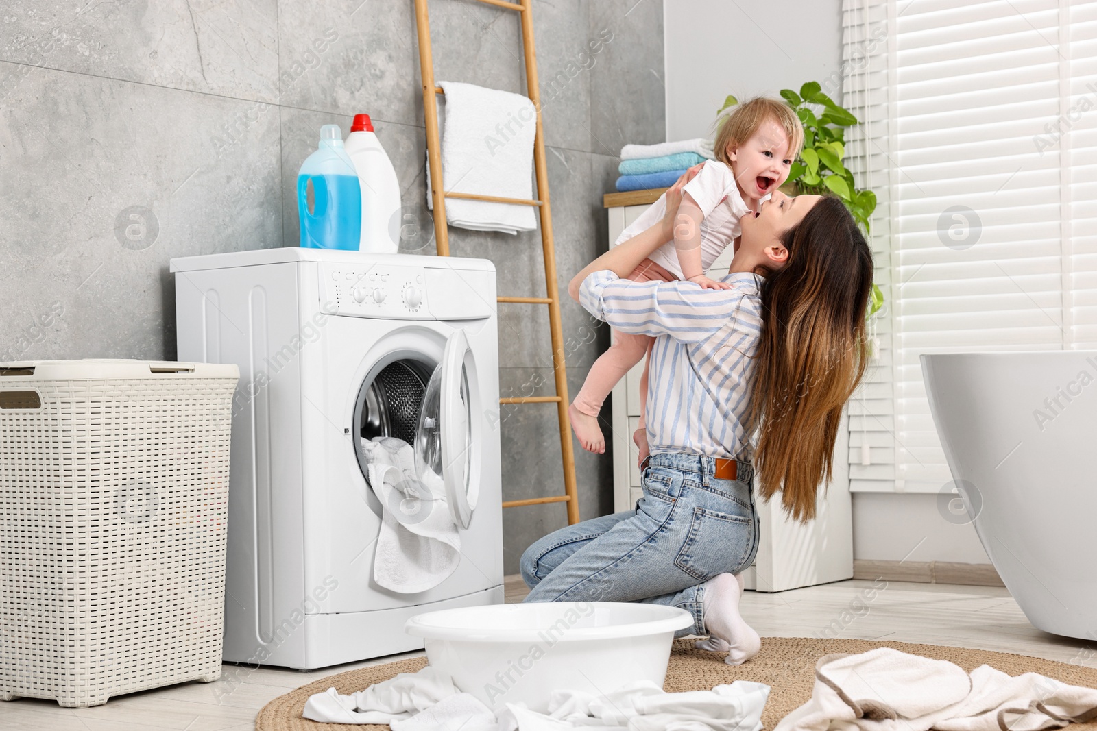 Photo of Mother with her daughter having fun while washing baby clothes in bathroom