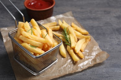 Photo of Tasty French fries, ketchup and rosemary on grey table, closeup