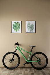 Modern green bicycle near beige wall indoors