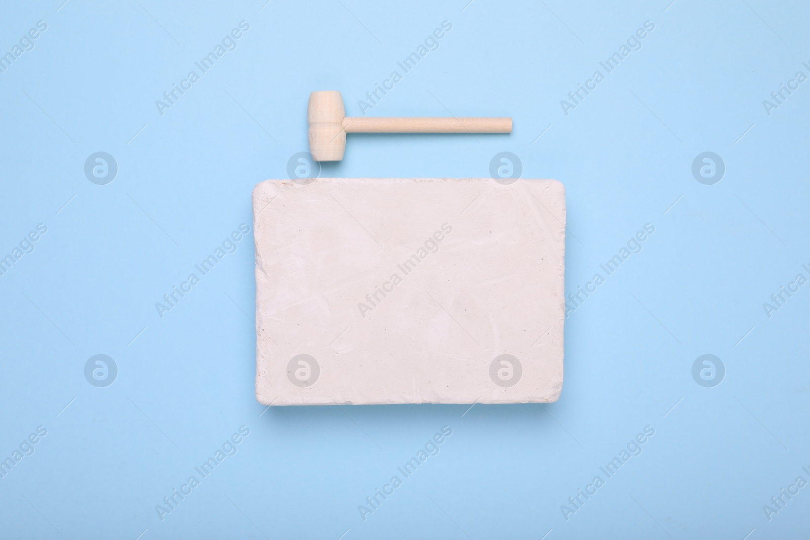 Photo of Educational toy for motor skills development. Excavation kit (plaster and wooden mallet) on light blue background, top view