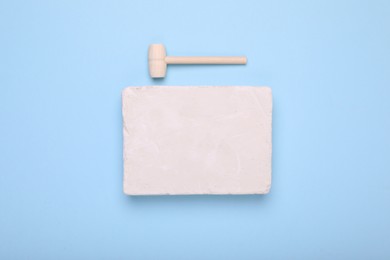 Photo of Educational toy for motor skills development. Excavation kit (plaster and wooden mallet) on light blue background, top view