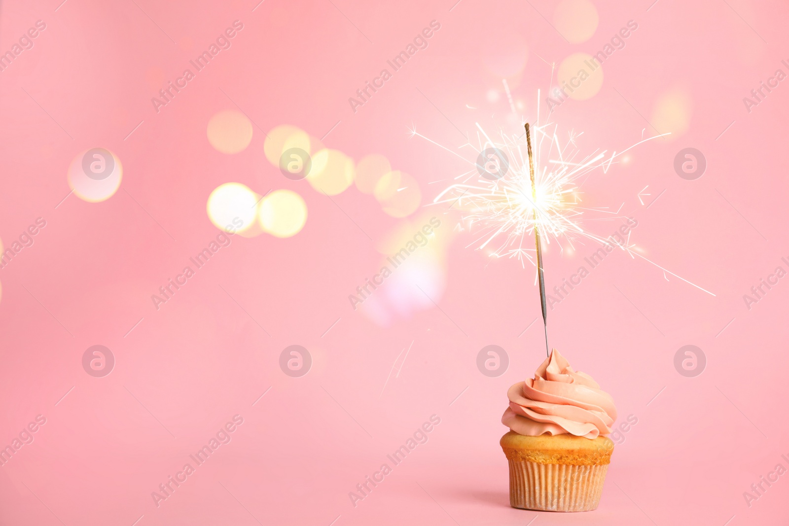 Image of Birthday cupcake with sparkler on pink background. Space for text