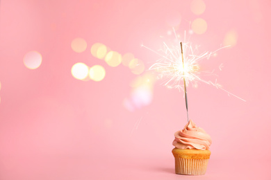 Image of Birthday cupcake with sparkler on pink background. Space for text