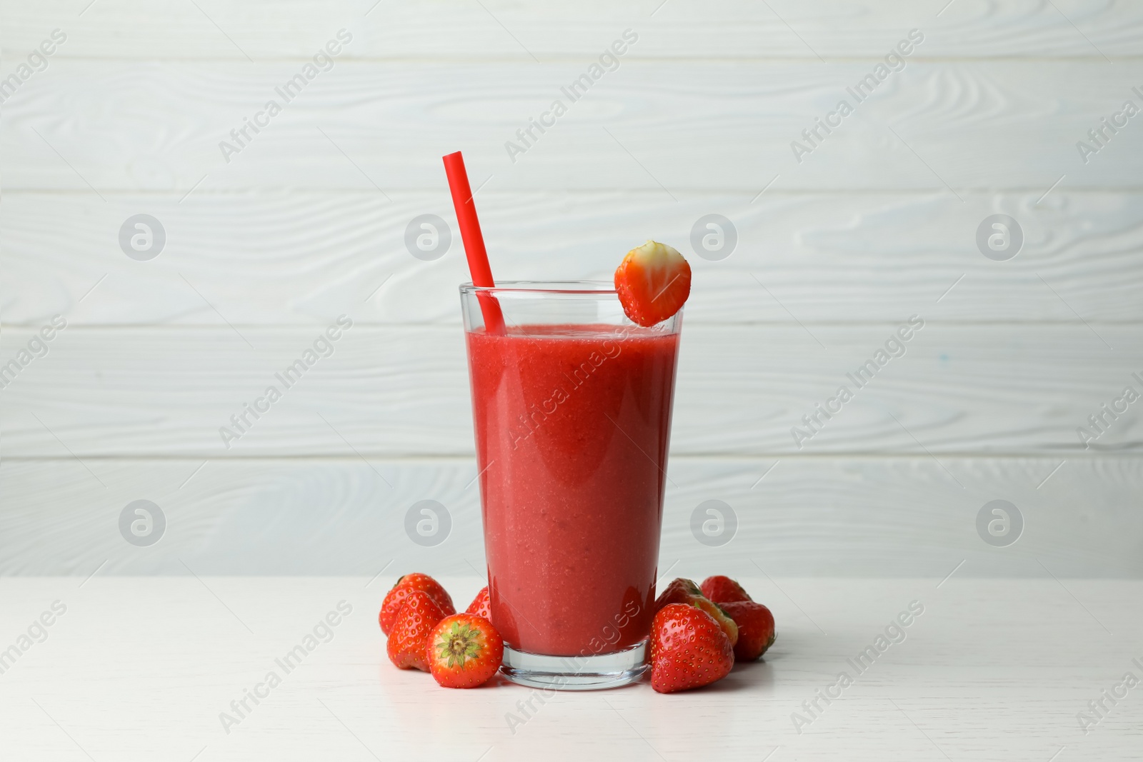 Photo of Glass with delicious berry smoothie and fresh strawberries on white wooden table