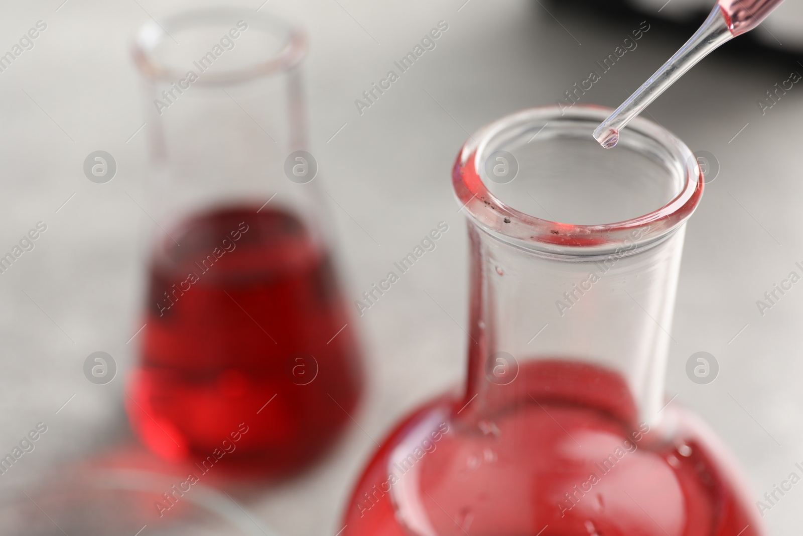 Photo of Laboratory analysis. Dripping red liquid into flask at light grey table, closeup