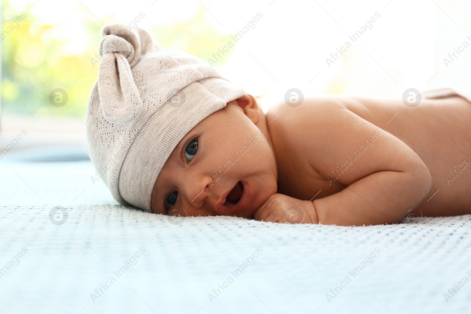 Photo of Cute little baby in hat lying on light blue plaid indoors