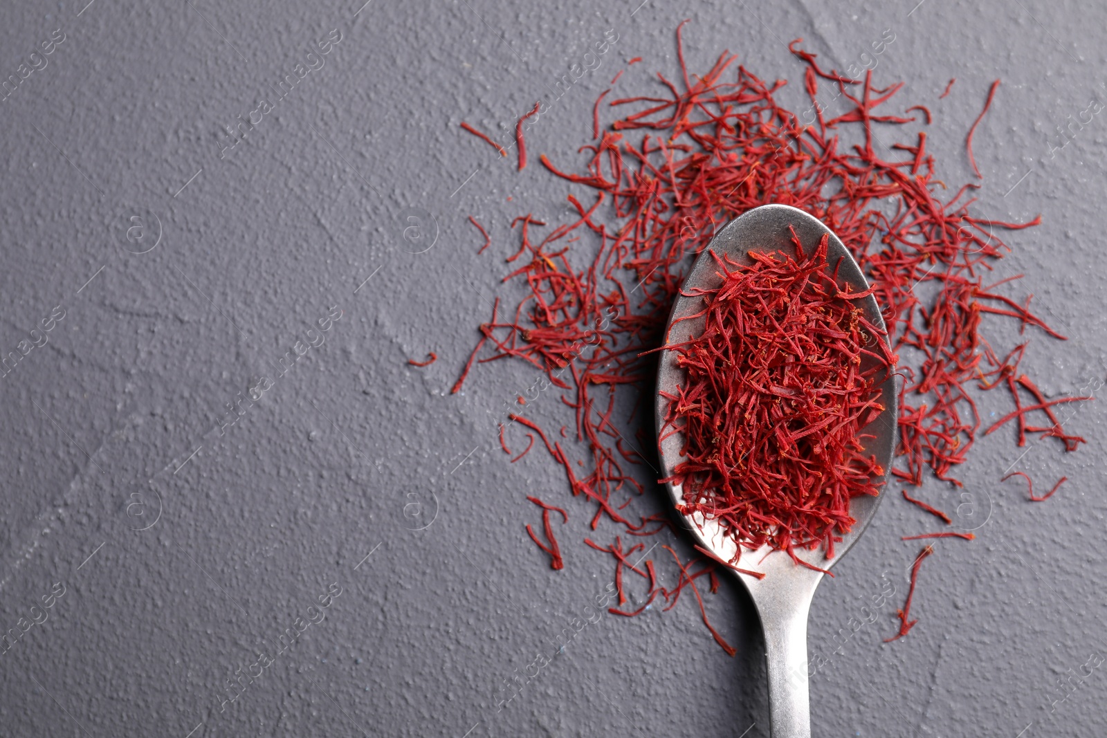 Photo of Aromatic saffron and spoon on gray table, top view. Space for text