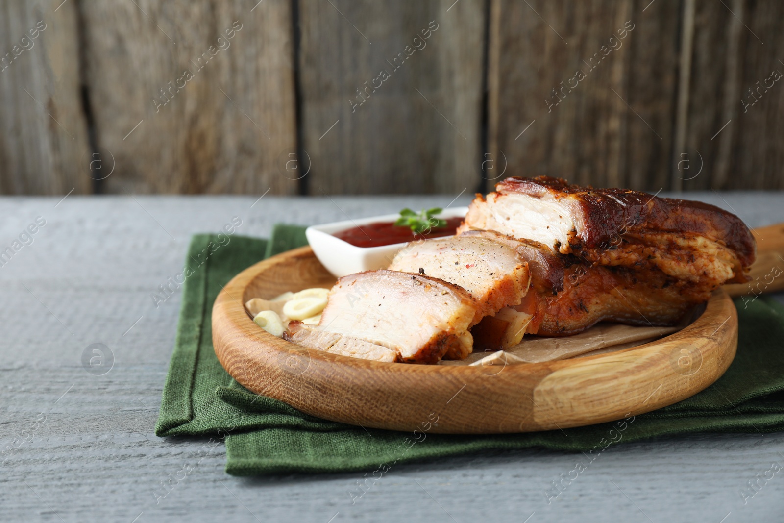 Photo of Pieces of baked pork belly served with sauce on grey wooden table, space for text