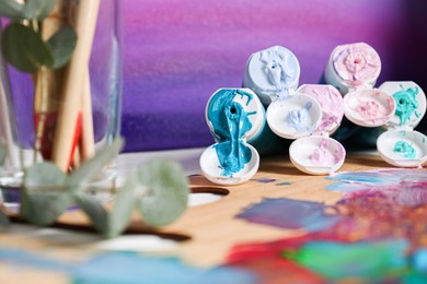 Wooden artist's palette and colorful paints on table, closeup