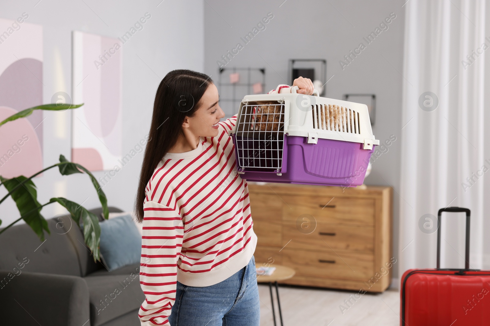 Photo of Travelling with pet. Smiling woman looking at carrier with her dog indoors