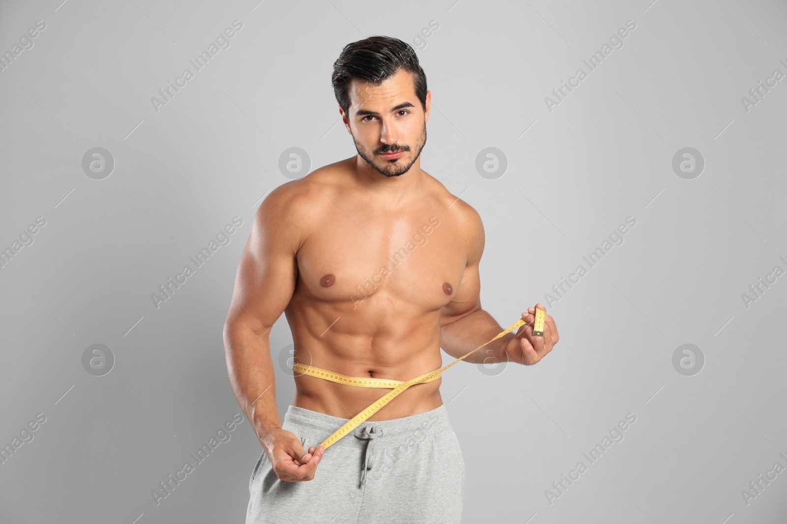 Photo of Young man with slim body using measuring tape on grey background