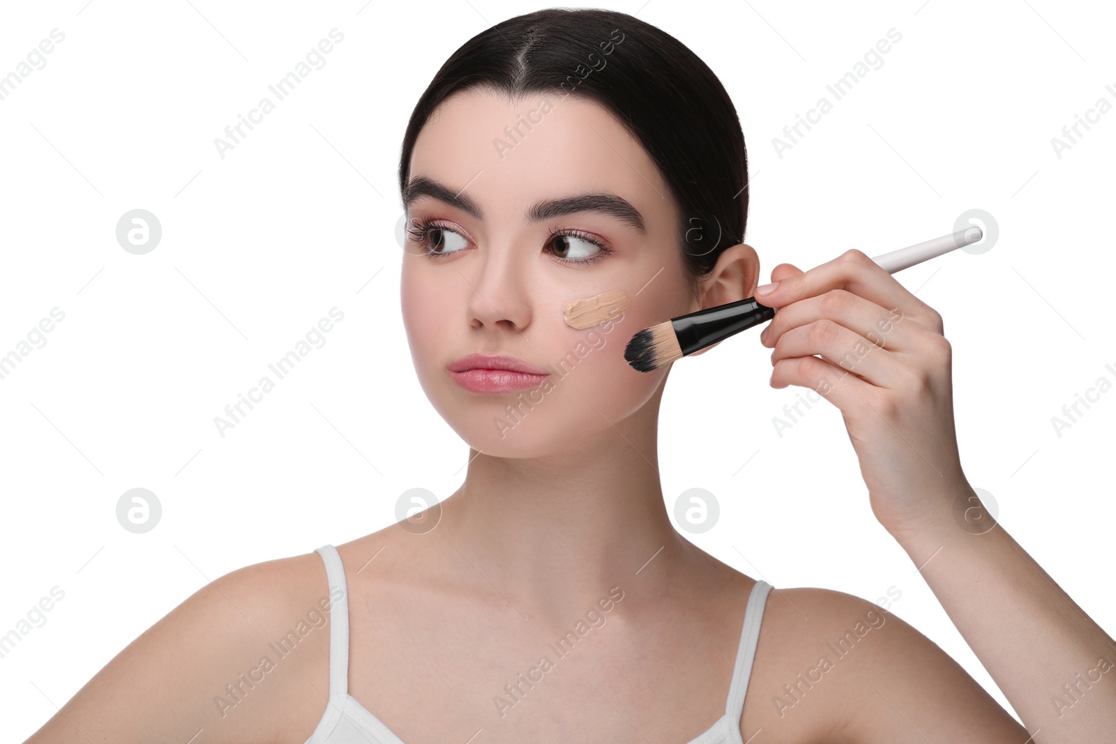 Photo of Teenage girl applying foundation on face with brush against white background