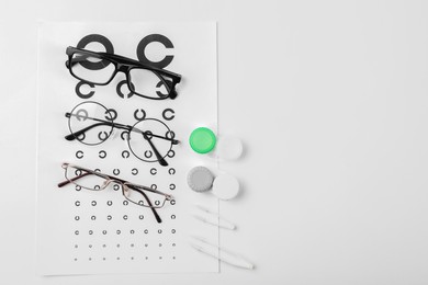 Photo of Vision test chart, glasses, lenses and tweezers on white background, flat lay. Space for text
