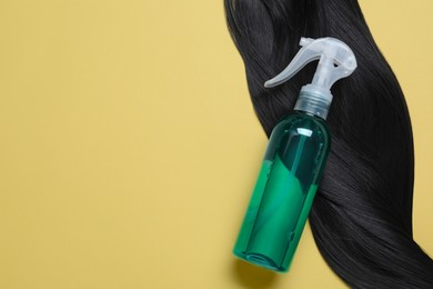 Photo of Spray bottle with thermal protection and lockblack hair on yellow background, flat lay. Space for text
