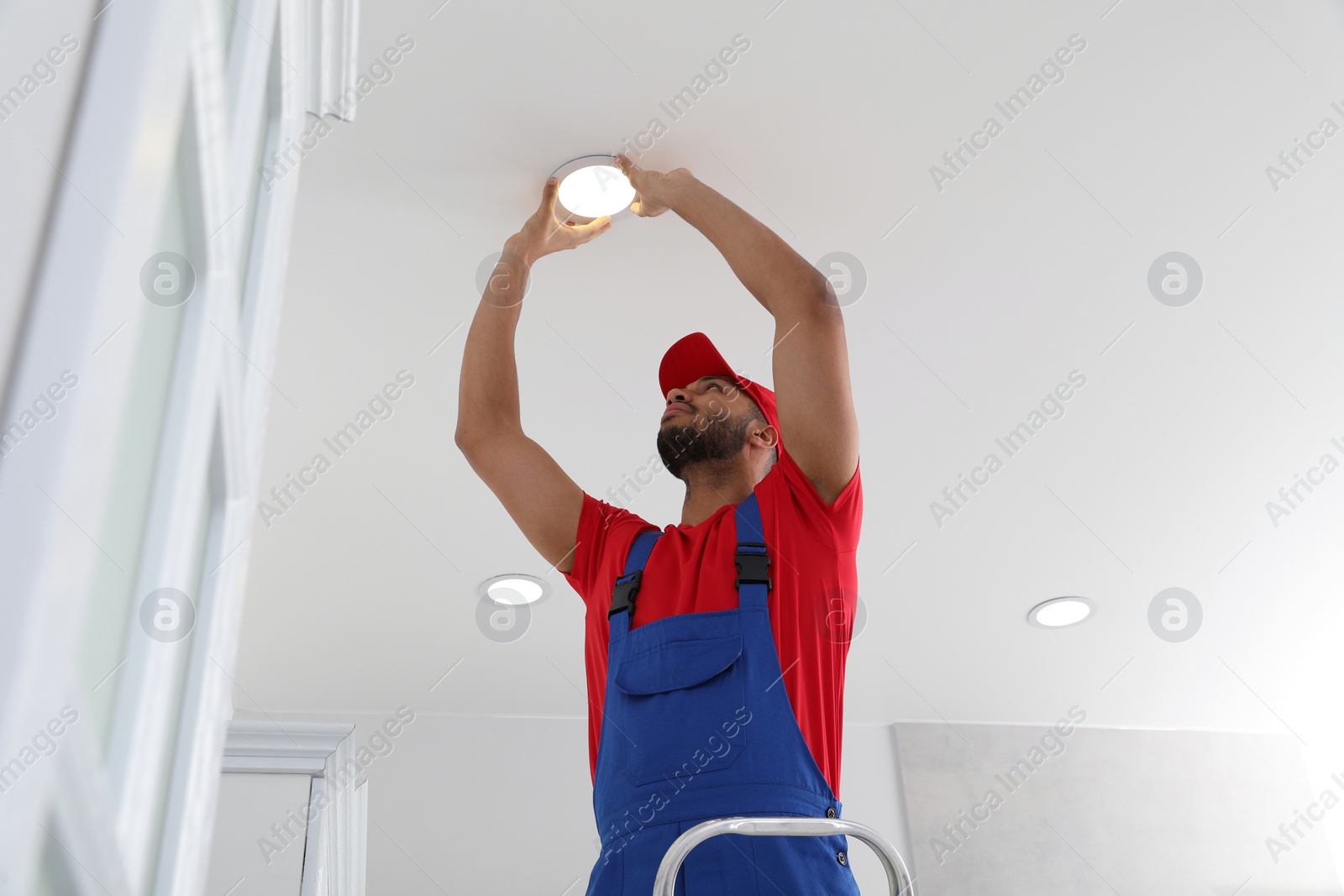 Photo of Electrician repairing ceiling lamp indoors, low angle view