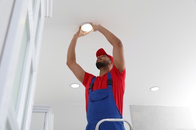 Photo of Electrician repairing ceiling lamp indoors, low angle view