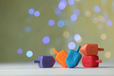 Photo of Hanukkah celebration. Dreidels with jewish letters against pale yellow background with blurred lights, closeup