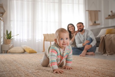 Photo of Happy parents watching their baby crawl on floor at home